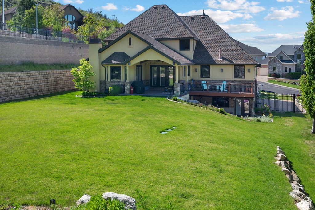Back of house with a lawn, a wooden deck, fence, stone siding, and stucco siding
