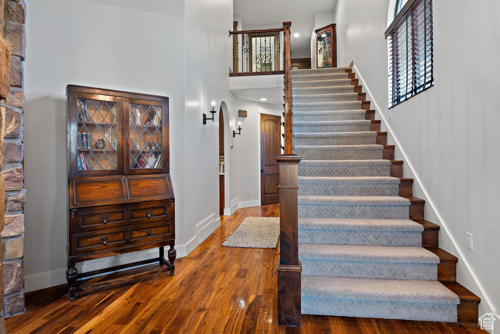 Stairs featuring visible vents, a towering ceiling, wood finished floors, baseboards, and arched walkways