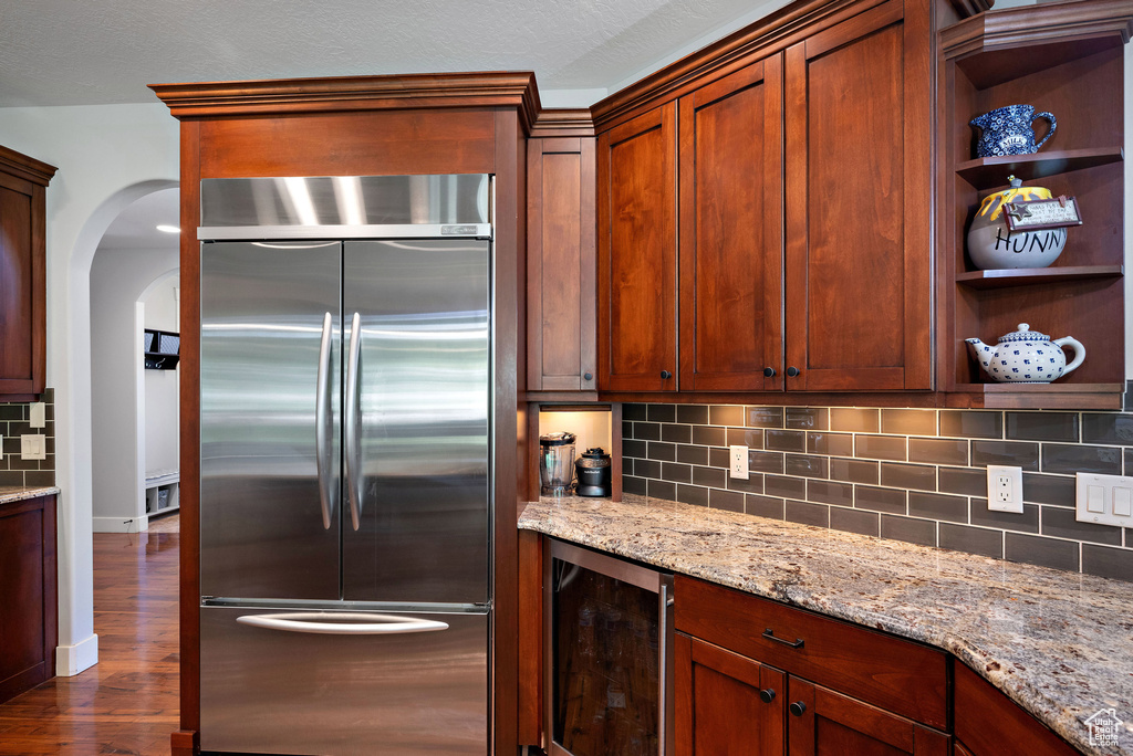Kitchen with arched walkways, stainless steel built in fridge, tasteful backsplash, wine cooler, and dark wood-style floors
