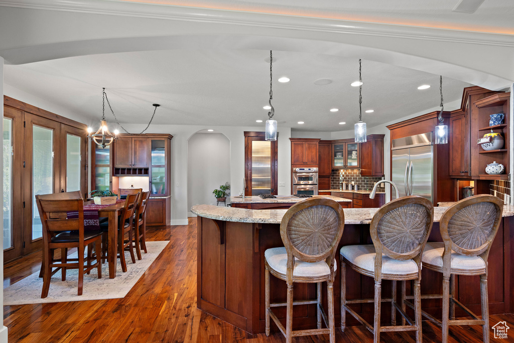 Kitchen with open shelves, appliances with stainless steel finishes, a breakfast bar area, arched walkways, and decorative light fixtures