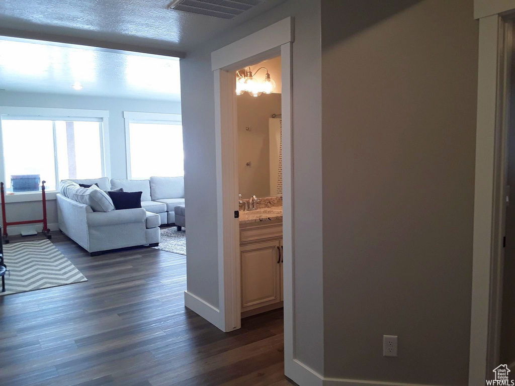 Hall featuring baseboards, visible vents, dark wood-style flooring, a textured ceiling, and a sink