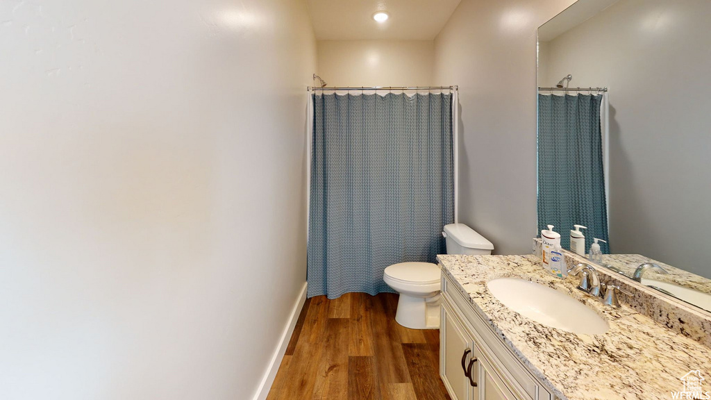 Bathroom with toilet, wood finished floors, vanity, baseboards, and a shower with curtain