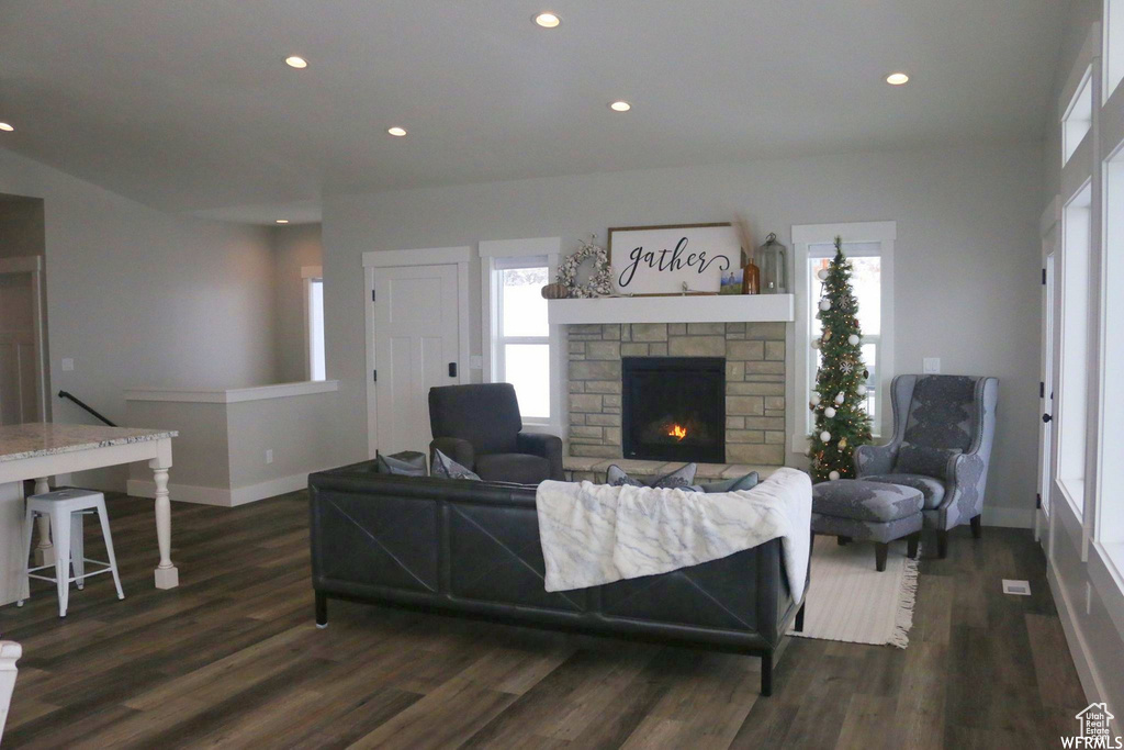 Living room featuring a stone fireplace, baseboards, dark wood-type flooring, and recessed lighting