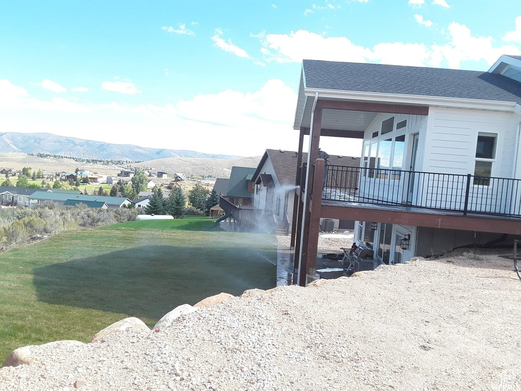 View of property exterior featuring a deck with mountain view, a yard, and a shingled roof