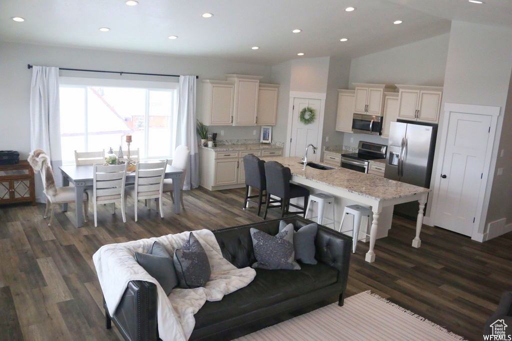 Kitchen featuring stainless steel appliances, a kitchen island with sink, a sink, light stone countertops, and a kitchen bar