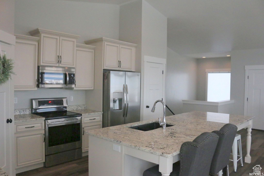 Kitchen with dark wood-style floors, appliances with stainless steel finishes, a breakfast bar area, and a sink