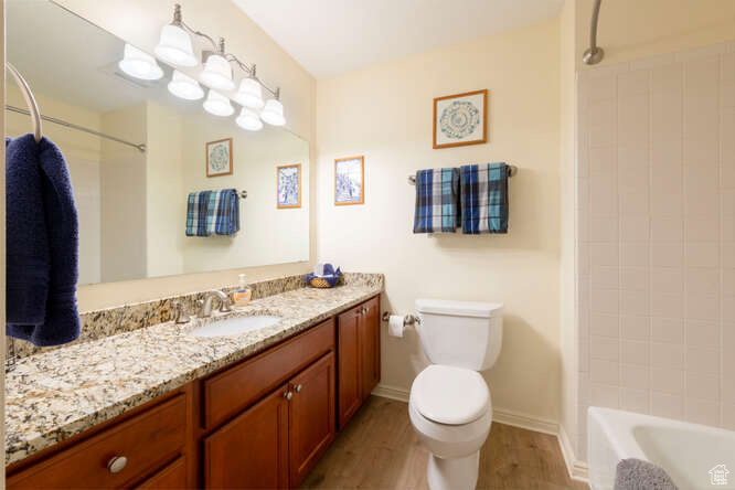 Bathroom with wood finished floors, toilet, vanity, baseboards, and shower / bathtub combination