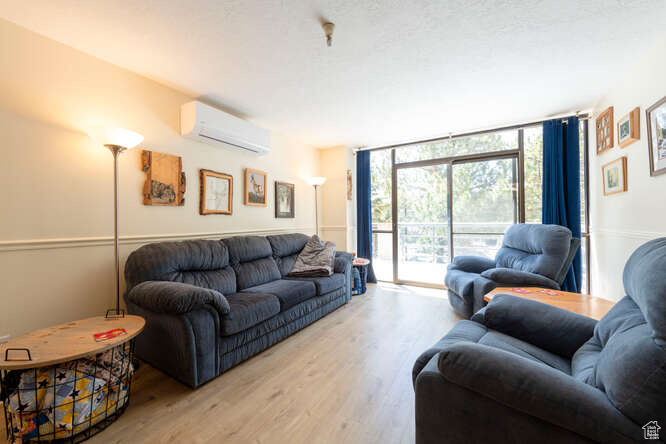 Living room with an AC wall unit, wood finished floors, and a wall of windows