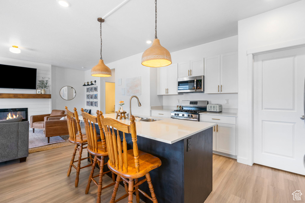 Kitchen featuring stainless steel appliances, a breakfast bar, a sink, light countertops, and light wood finished floors