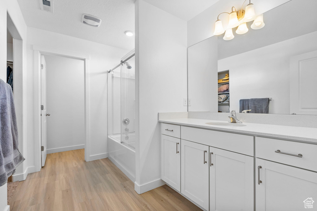 Bathroom featuring wood finished floors, vanity, bathing tub / shower combination, visible vents, and baseboards