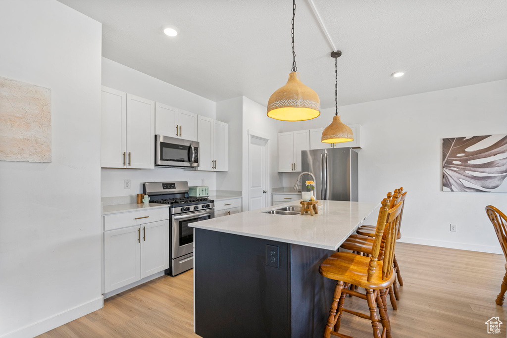 Kitchen with a sink, white cabinets, appliances with stainless steel finishes, light wood-type flooring, and a kitchen bar