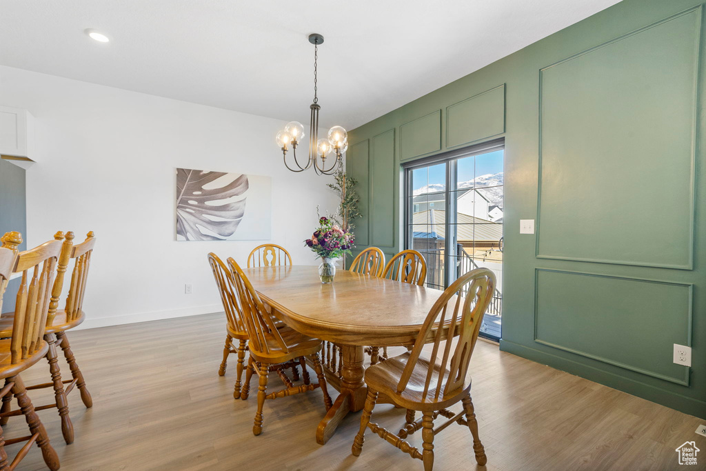 Dining space featuring a notable chandelier, light wood-style floors, baseboards, and a decorative wall