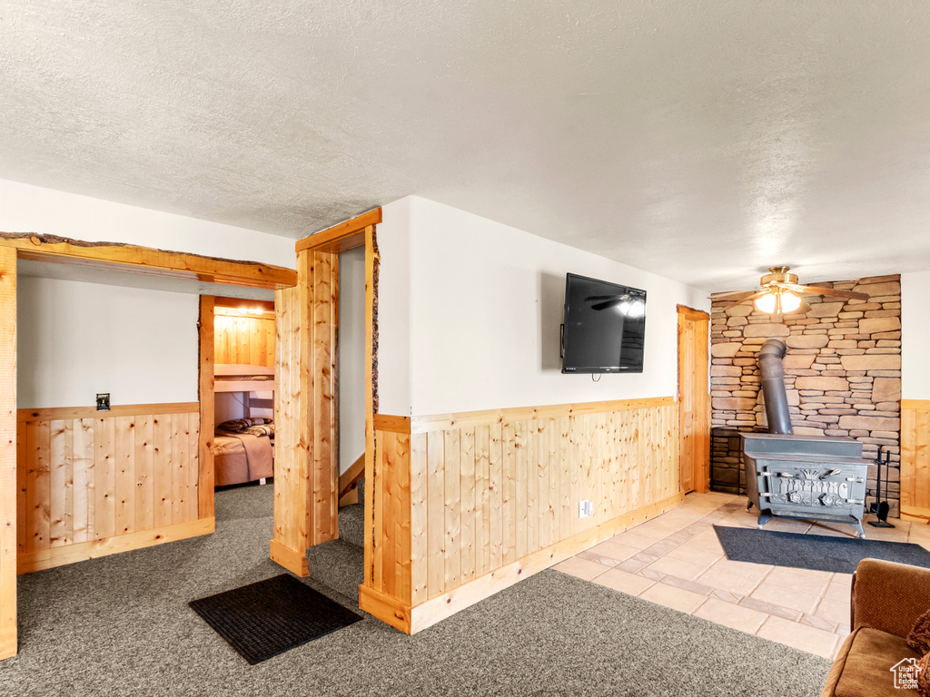 Living room with a wood stove, wood walls, wainscoting, a textured ceiling, and ceiling fan