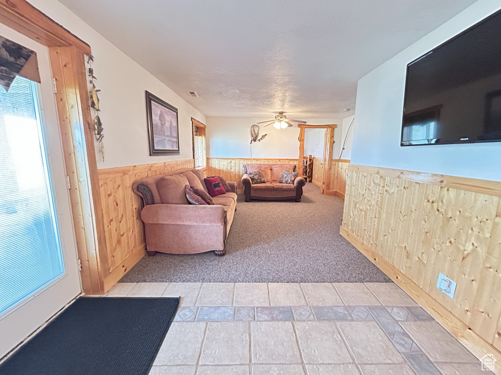 Living area with a wainscoted wall, wooden walls, ceiling fan, light carpet, and light tile patterned floors