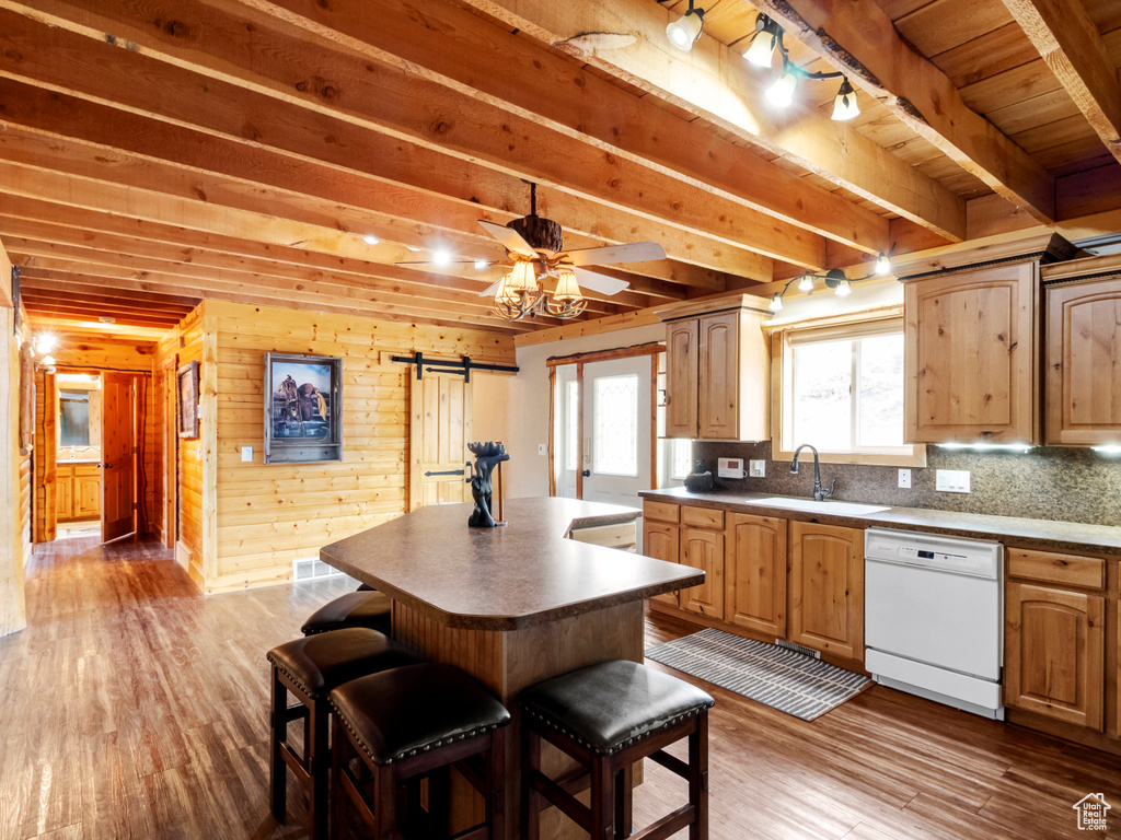 Kitchen featuring white dishwasher, a sink, a barn door, wood finished floors, and a center island