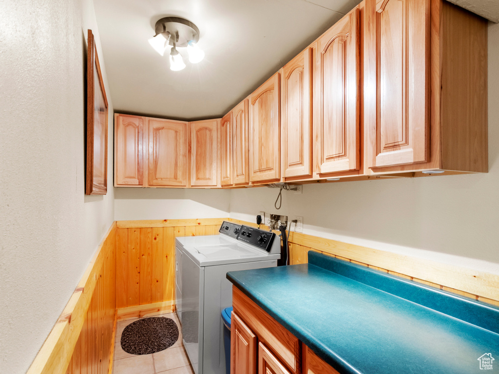 Laundry area featuring wood walls, independent washer and dryer, cabinet space, a wainscoted wall, and light tile patterned floors