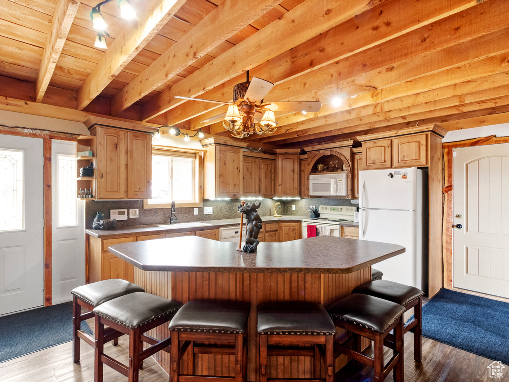 Kitchen featuring white appliances, a sink, backsplash, a kitchen bar, and beamed ceiling