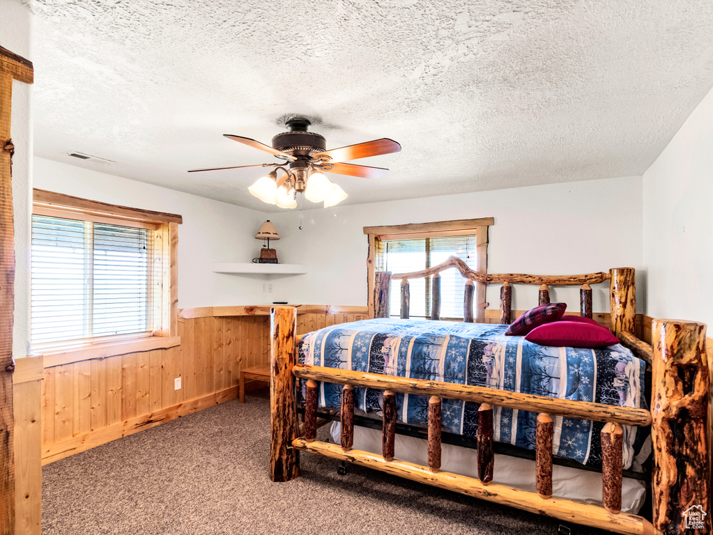Bedroom with a wainscoted wall, a textured ceiling, carpet flooring, wood walls, and ceiling fan