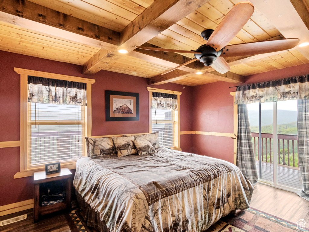 Bedroom with wooden ceiling with exposed beams, access to outside, multiple windows, wood finished floors, and a ceiling fan