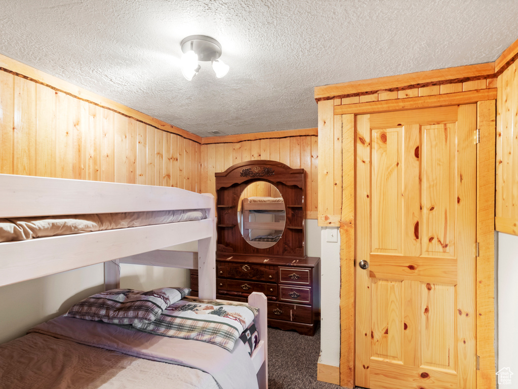 Carpeted bedroom featuring a textured ceiling and wooden walls