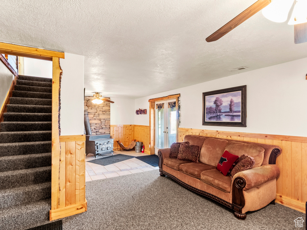 Carpeted living area featuring ceiling fan, a wainscoted wall, wooden walls, a wood stove, and stairs