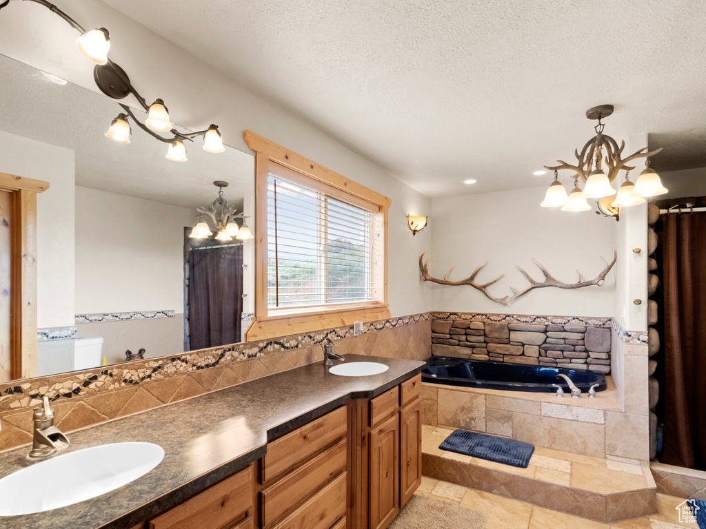 Full bathroom featuring a chandelier, a garden tub, double vanity, decorative backsplash, and a textured ceiling