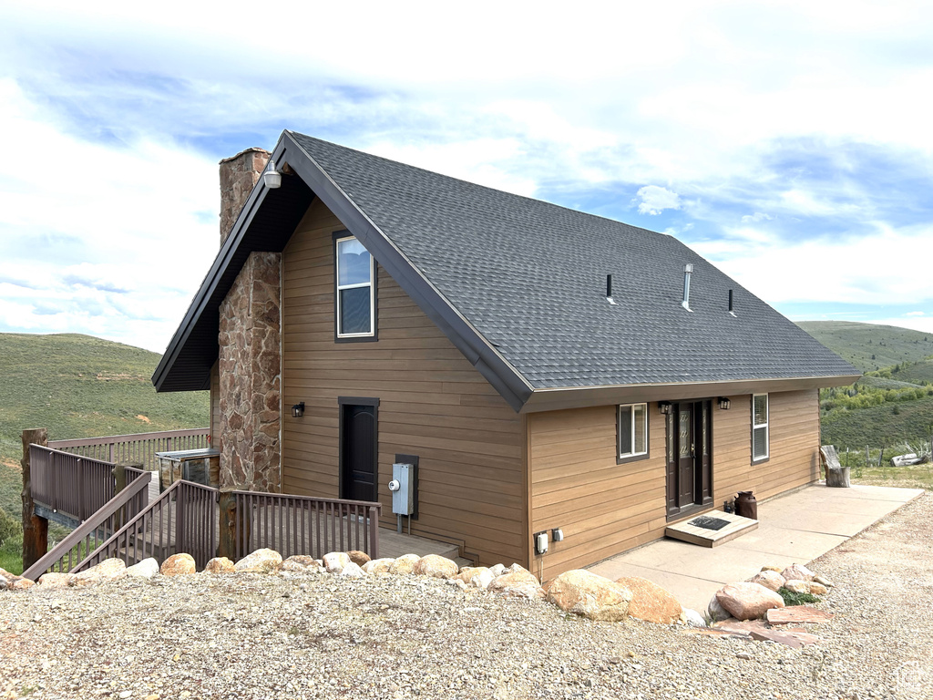 Back of property with a chimney, a shingled roof, a wooden deck, and a patio area