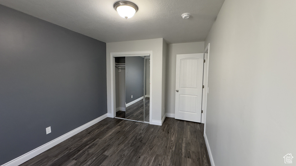 Unfurnished bedroom featuring dark wood-type flooring, a closet, a textured ceiling, and baseboards