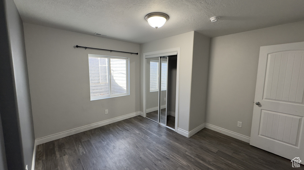 Unfurnished bedroom with baseboards, visible vents, dark wood-style flooring, a textured ceiling, and a closet