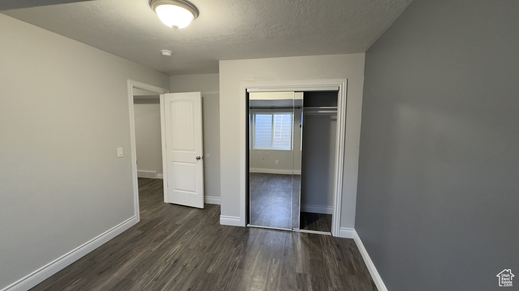 Unfurnished bedroom with a textured ceiling, dark wood-style flooring, visible vents, baseboards, and a closet