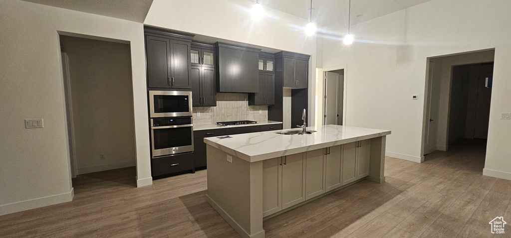 Kitchen with a center island with sink, light wood finished floors, stainless steel appliances, backsplash, and glass insert cabinets