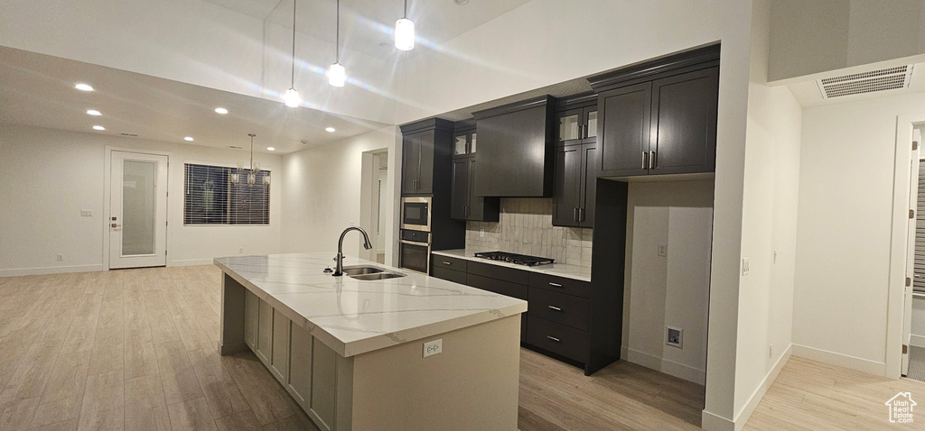 Kitchen featuring a center island with sink, visible vents, stainless steel appliances, light wood-style floors, and a sink