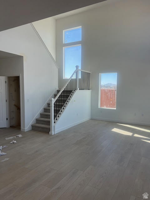 Unfurnished living room featuring stairs, wood finished floors, a towering ceiling, and baseboards