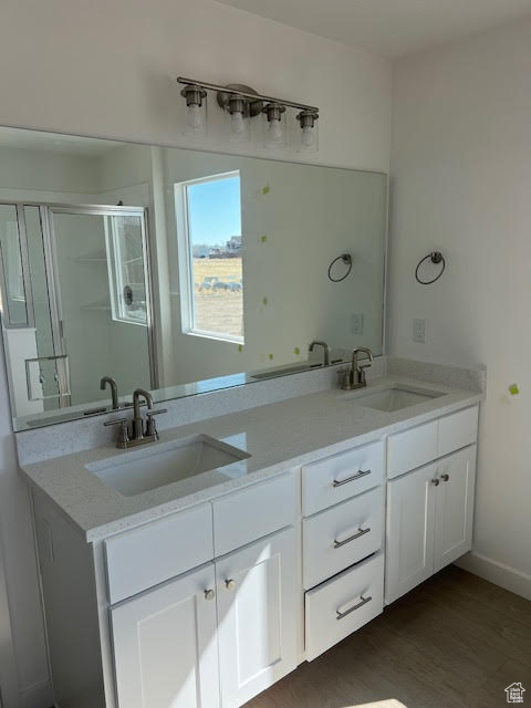 Full bathroom with double vanity, a shower stall, a sink, and wood finished floors