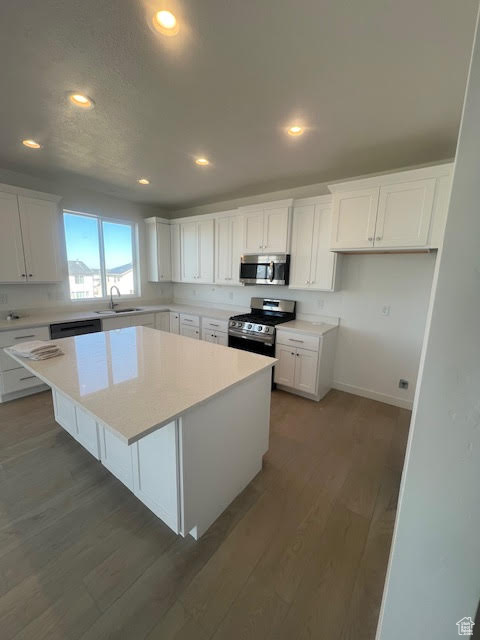 Kitchen featuring appliances with stainless steel finishes, wood finished floors, a center island, white cabinetry, and a sink