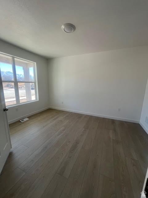 Unfurnished room featuring dark wood-style floors, visible vents, and baseboards