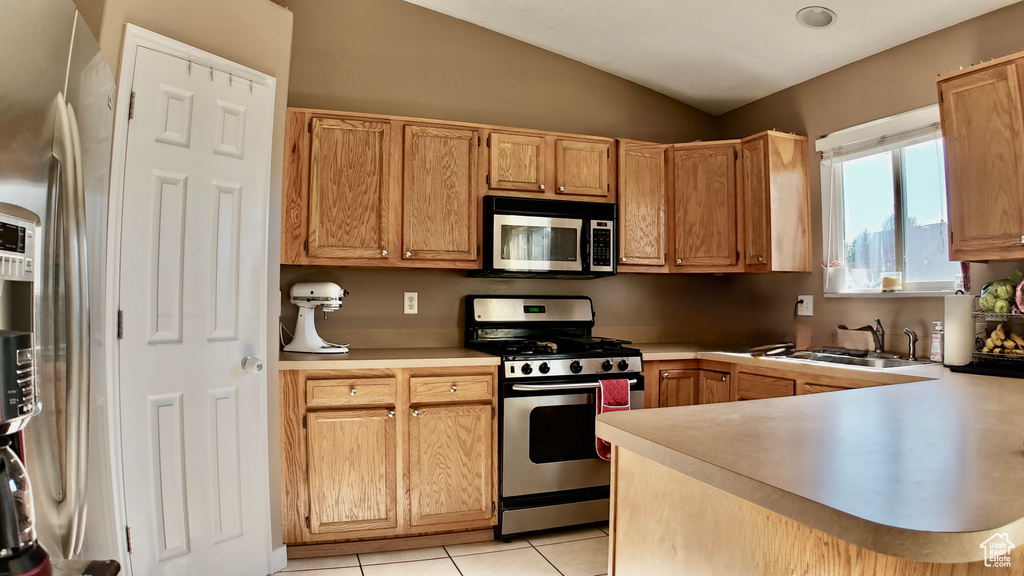 Kitchen featuring appliances with stainless steel finishes, a sink, vaulted ceiling, light countertops, and light tile patterned floors