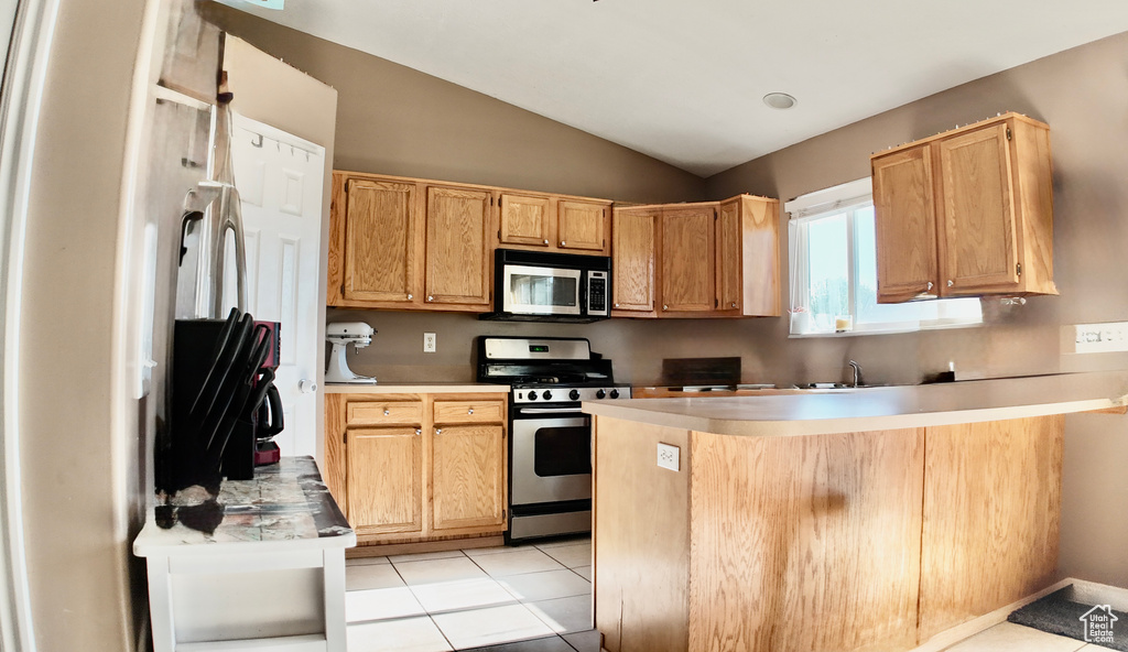 Kitchen featuring appliances with stainless steel finishes, vaulted ceiling, a peninsula, a sink, and light countertops
