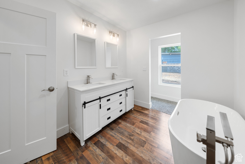 Bathroom featuring double vanity, a freestanding bath, and wood finished floors