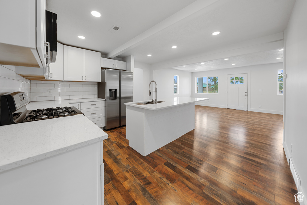 Kitchen with stainless steel refrigerator with ice dispenser, range with gas stovetop, backsplash, dark wood-style flooring, and recessed lighting