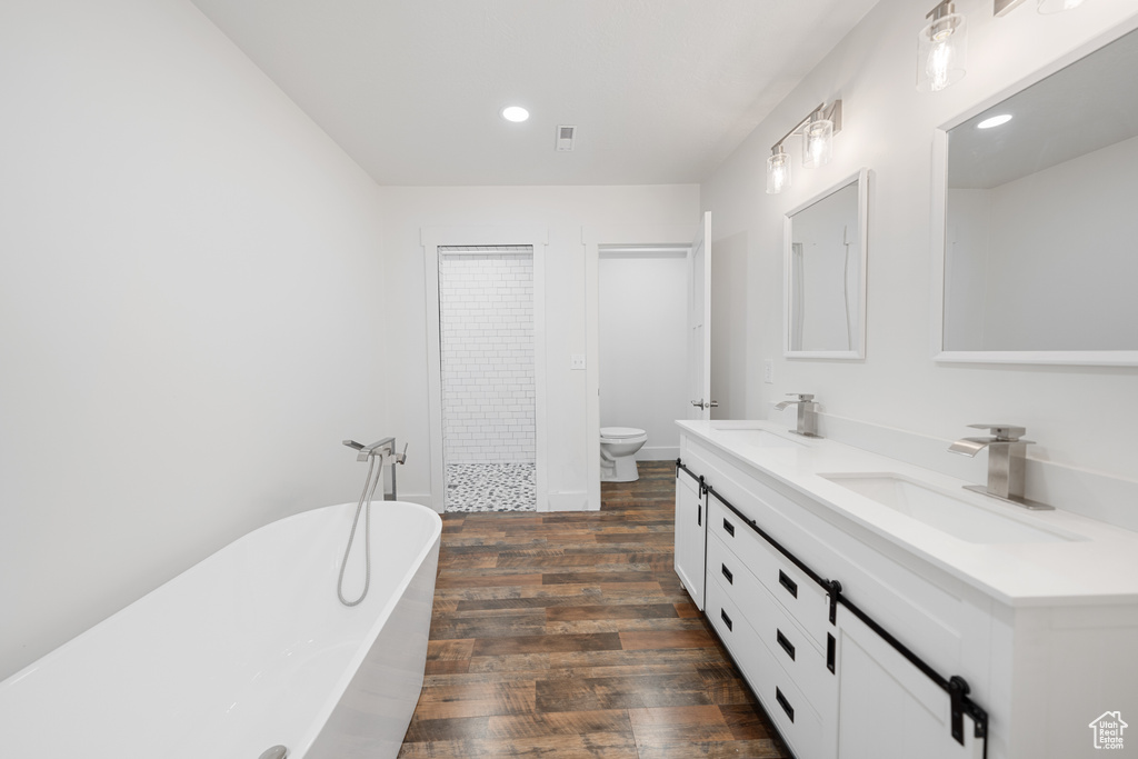 Bathroom featuring wood finished floors, double vanity, a soaking tub, recessed lighting, and tiled shower