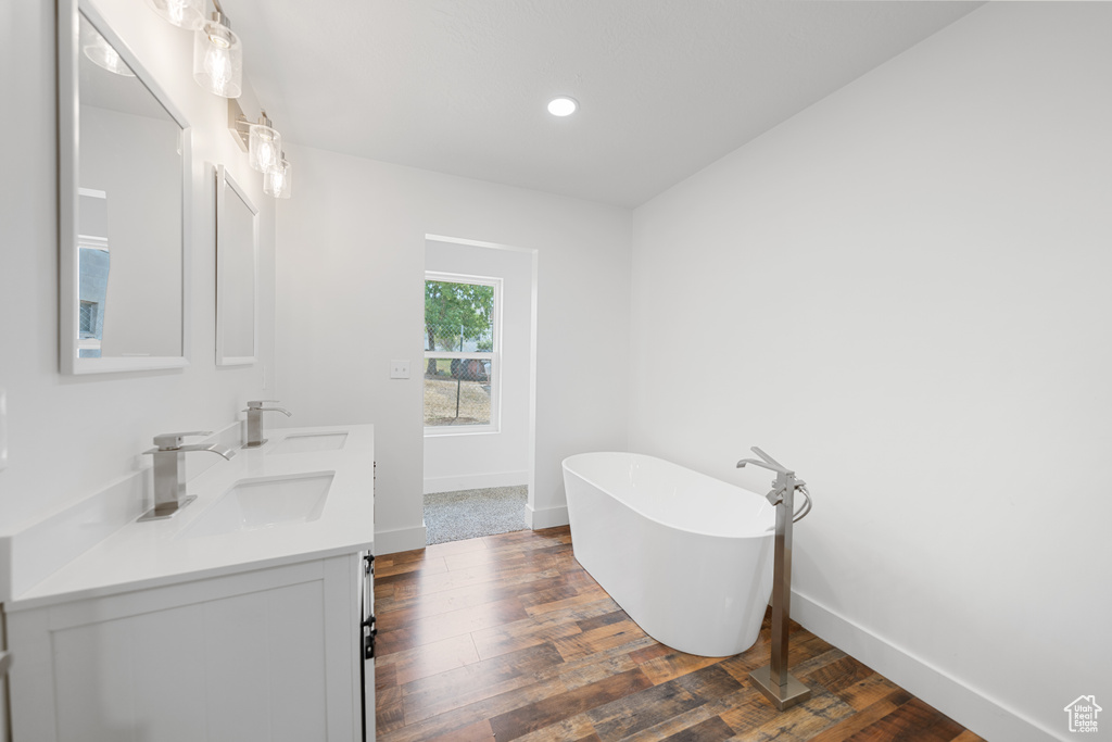 Full bathroom with a soaking tub, double vanity, wood finished floors, and recessed lighting
