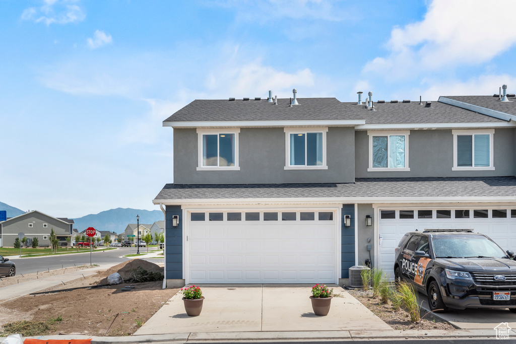 View of front of house with a mountain view, a garage, concrete driveway, roof with shingles, and stucco siding