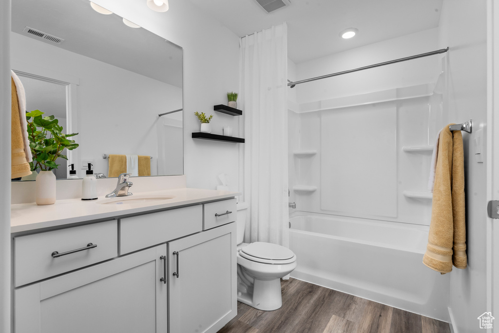 Full bath with visible vents, toilet, shower / tub combo, vanity, and wood finished floors