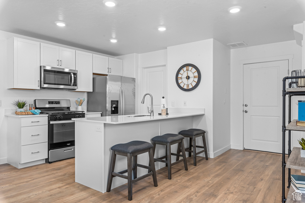 Kitchen featuring white cabinets, a breakfast bar area, stainless steel appliances, light wood-type flooring, and a sink