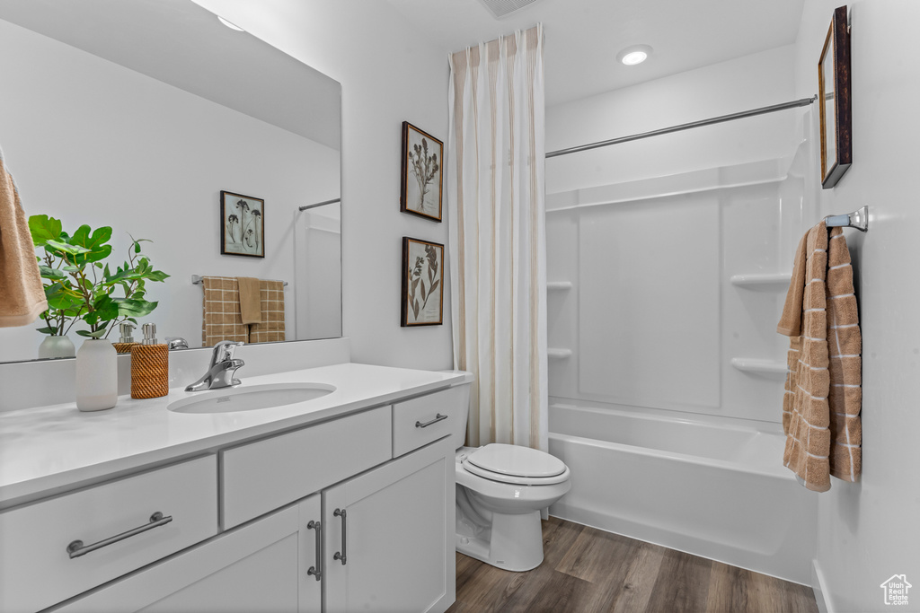 Full bath with vanity, shower / bath combo with shower curtain, wood finished floors, and toilet