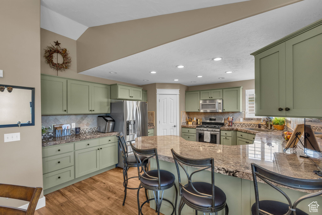 Kitchen with green cabinets, appliances with stainless steel finishes, a peninsula, a sink, and a kitchen bar