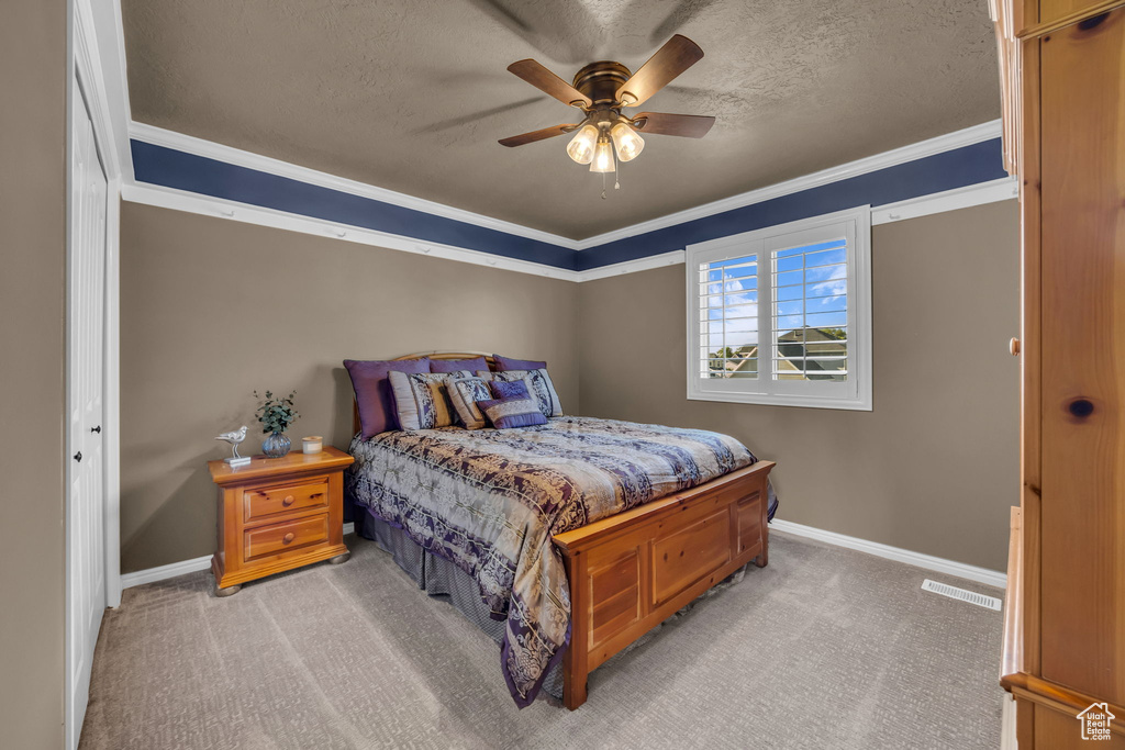Bedroom with light colored carpet, baseboards, a textured ceiling, crown molding, and a ceiling fan