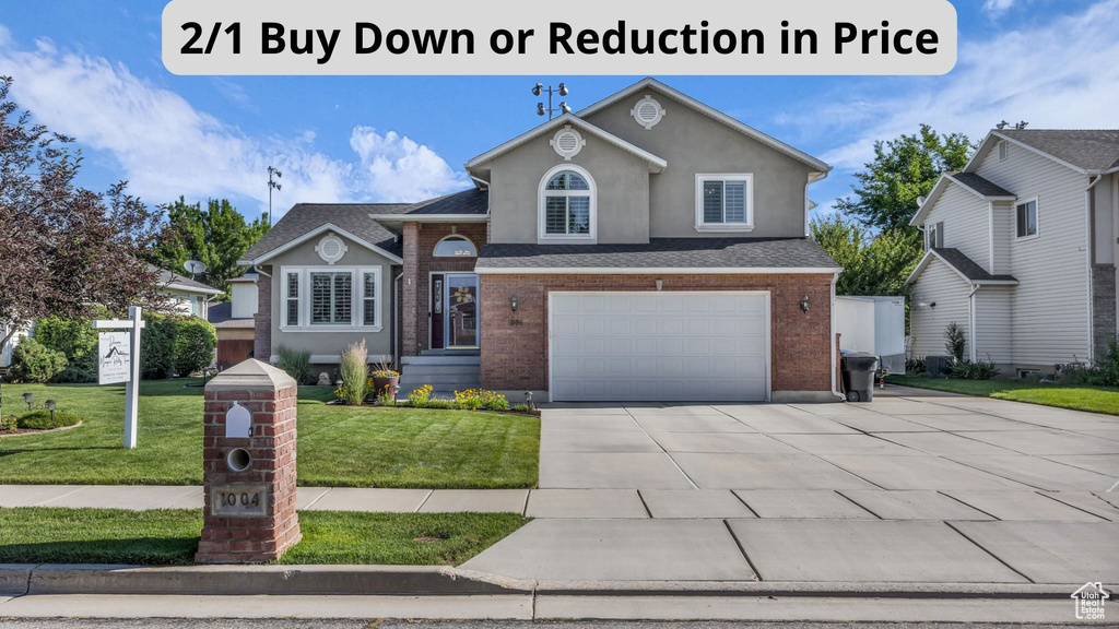 View of front of property with an attached garage, a front lawn, driveway, stucco siding, and brick siding