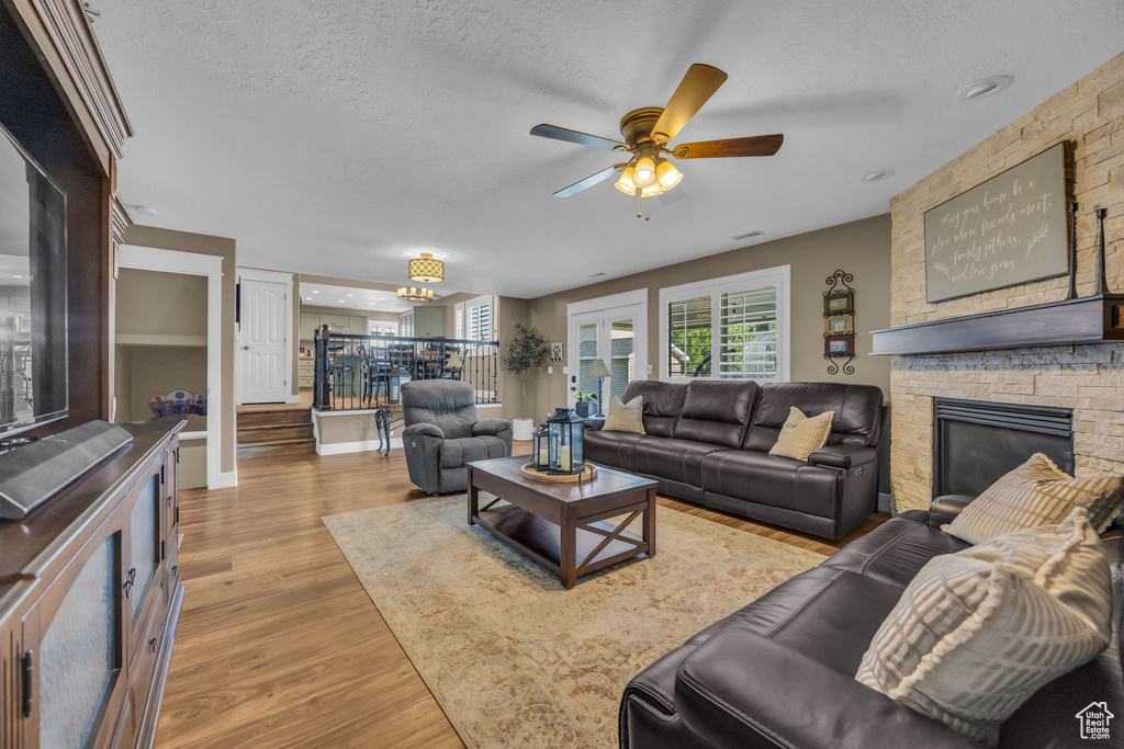 Living area with ceiling fan, a textured ceiling, wood finished floors, and a stone fireplace